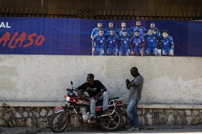 Two men rest in front of a banner of the Haitian national football team in Petion-ville, Port-au-Prince, Haiti, on April 14, 2026.