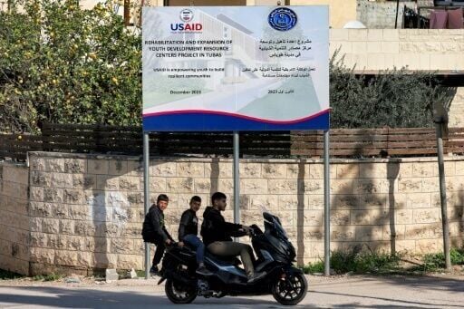 Boys ride behind a man on a scooter past a USAID-funded project for a youth center in Tubas in the north of the occupied West Bank on February 4, 2025
