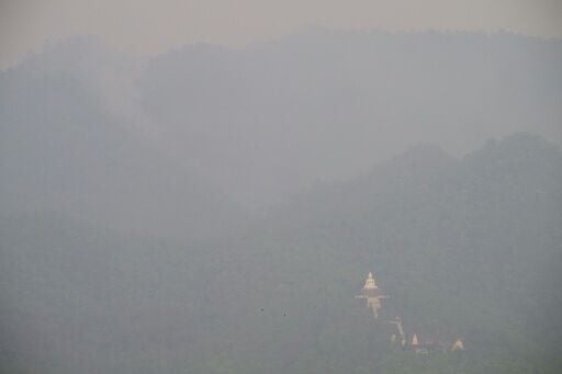 A white Buddha statue shrouded in heavy pollution as smoke rises from a hillside wildfire in Pai, west of Chiang Mai