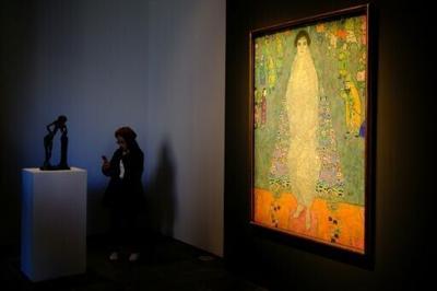 The piece represents the daughter of Klimt's main patron dressed in a white imperial Chinese dress, standing before a blue tapestry with Asian-inspired motifs