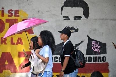 People walk past a mural depicting now ousted Venezuelan president Nicolas Maduro near the National Assembly in Caracas