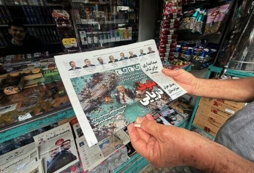 A man looks at the front page of the Jam Jam newspaper on sale at a newsstand in Tehran, featuring a cartoon of US President Donald Trump drowning in the Strait of Hormuz with the headline “Marine Bluff”