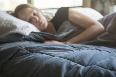 Young redhead woman using soft weighted blanket in her modern apartment