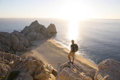 Man looks out across beach and sea from rock cliffs