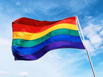 Rainbow flag waving in the wind against blue sky