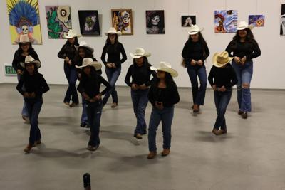 People dancing wearing hats and jeans with paintings in the background. 