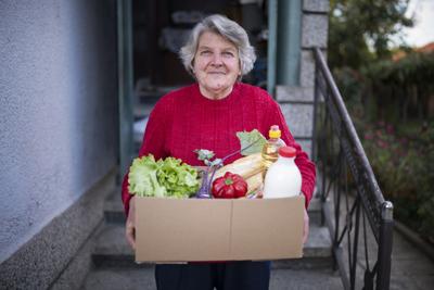 Portrait of happy senior woman with received crate with food during pandemic.