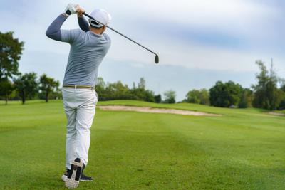 Golfer hitting golf ball along fairway with iron driver