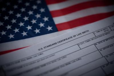 U.S. standard certificate of live birth application form next to flag of USA. Birthright citizenship concept.