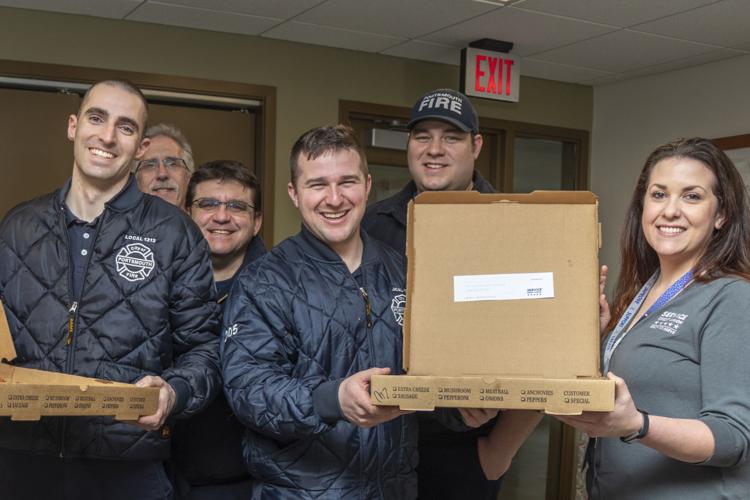 Service Credit Union's Jaime Yates (r.) presents a surprise pizza delivery to Portsmouth firefighters.
