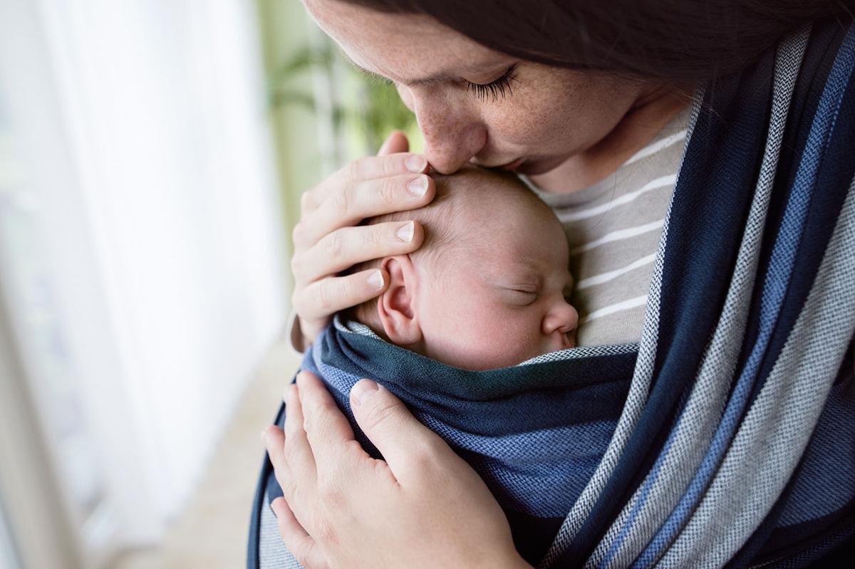 Close up, beautiful mother kissing her son in sling