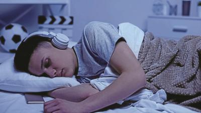 Male teenage boy fallen asleep in headphones, overworked student relaxing