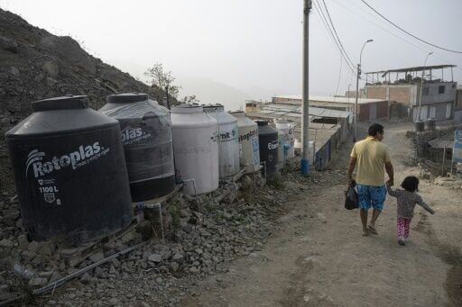 A man walks with his daughter next to water drums on the southern outskirts of Lima on March 13, 2025