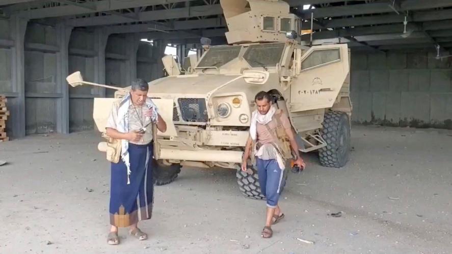 An armed man walks next to an armoured vehicle, in Mocha