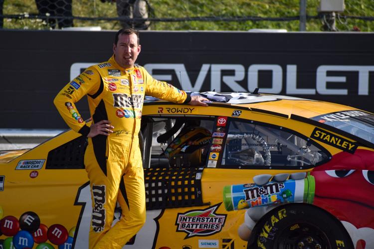 Kyle Busch poses with his No. 18 M&M's Toyota after winning the Explore the Pocono Mountains 350 Cup Series race at Pocono
