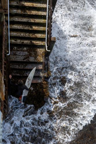 A surfer makes her exit from the beach during high tide at a closed beach access stairway in Encinitas