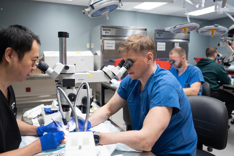 On left, Weifeng Zeng, senior scientist of UW Microsurgery, practices repairing blood vessels in a chicken thigh with Ukrainian surgeons at the UW Microsurgery Regenerative Medicine Lab in Madison in April. The plastic surgery division hosted six Ukrainian