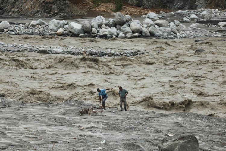 People walk by the banks of the River Trishuli after mudslides, in Trishuli