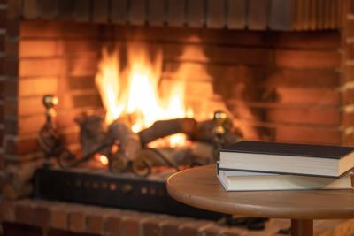 Books stacked on a small table in front of a fireplace with fire in winter.