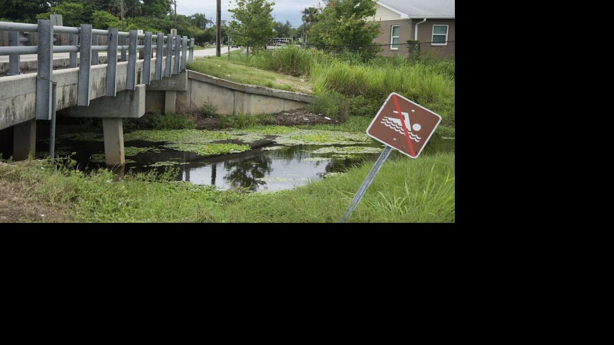 Billy's Creek canal running under a bridge in Fort Myers with a crooked no swimming sign.JPEG