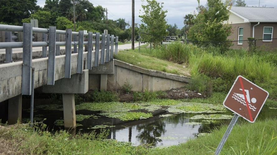 Billy's Creek canal running under a bridge in Fort Myers with a crooked no swimming sign.JPEG