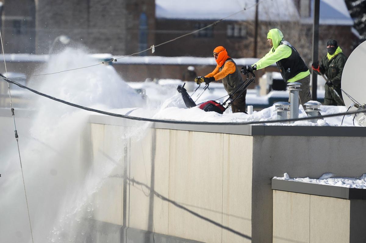 A team of snowblowers work to clear snow off the roof of the downtown post office