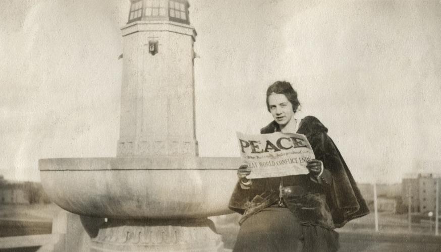 An unidentified woman seated on the Confederate Fountain in Helena holding up a newspaper with "PEACE" headline after the end of World War I.