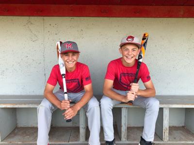 Tommy Woodcock(left) and Ethan Garner smile with their bats in the dugout.