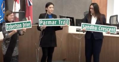 Beth Robertson, Pavan Parmar and Jasvinder Sandhu hold novelty street signs with their surnames on them