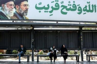 Iranians wait at a bus stop as they sit under a banner featuring Iran's late supreme leaders Ayatollah Ali Khamenei (L) and his son newly elected supreme leader Mojtaba Khamenei, in northern Tehran