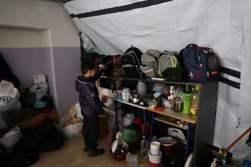 A displaced child retrieves his school bag with his books before his online class