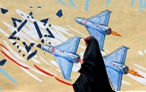 A woman walks past an anti-US and anti-Israel mural in Tehran
