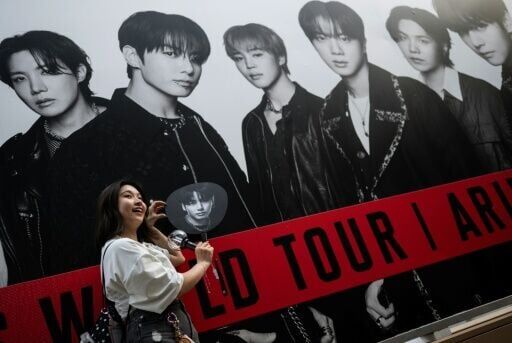 A fan of Korean boy band BTS poses for a photo in front of a poster at Tokyo Dome