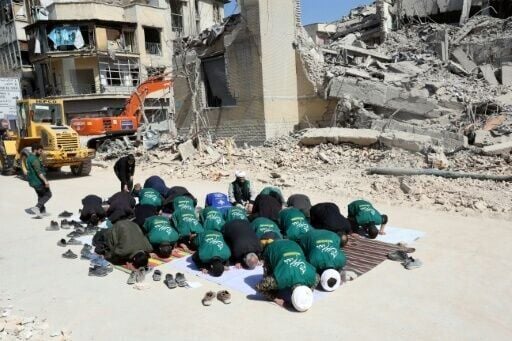 Iranian clerics and volunteers from the Basij paramilitary group pray next to the rubble of a destroyed police station in Tehran on March 4