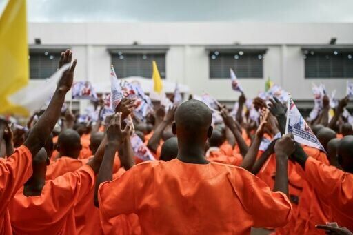 Inmates pray and wave flags bearing images commemorating the visit of Pope Leo XIV during his visit to Bata Prison