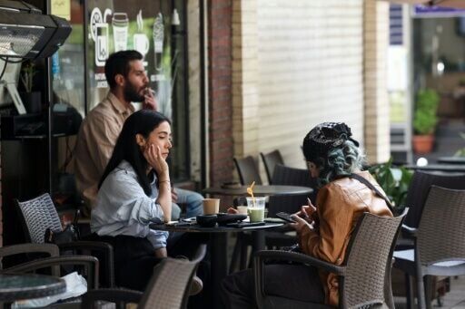 Two women sit at a cafe table with drinks in Tehran