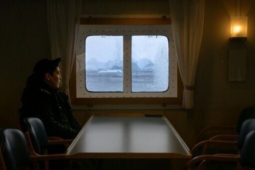 A man watches icebergs and mountains drift by the ship as it passes through Icefjord, Greenland