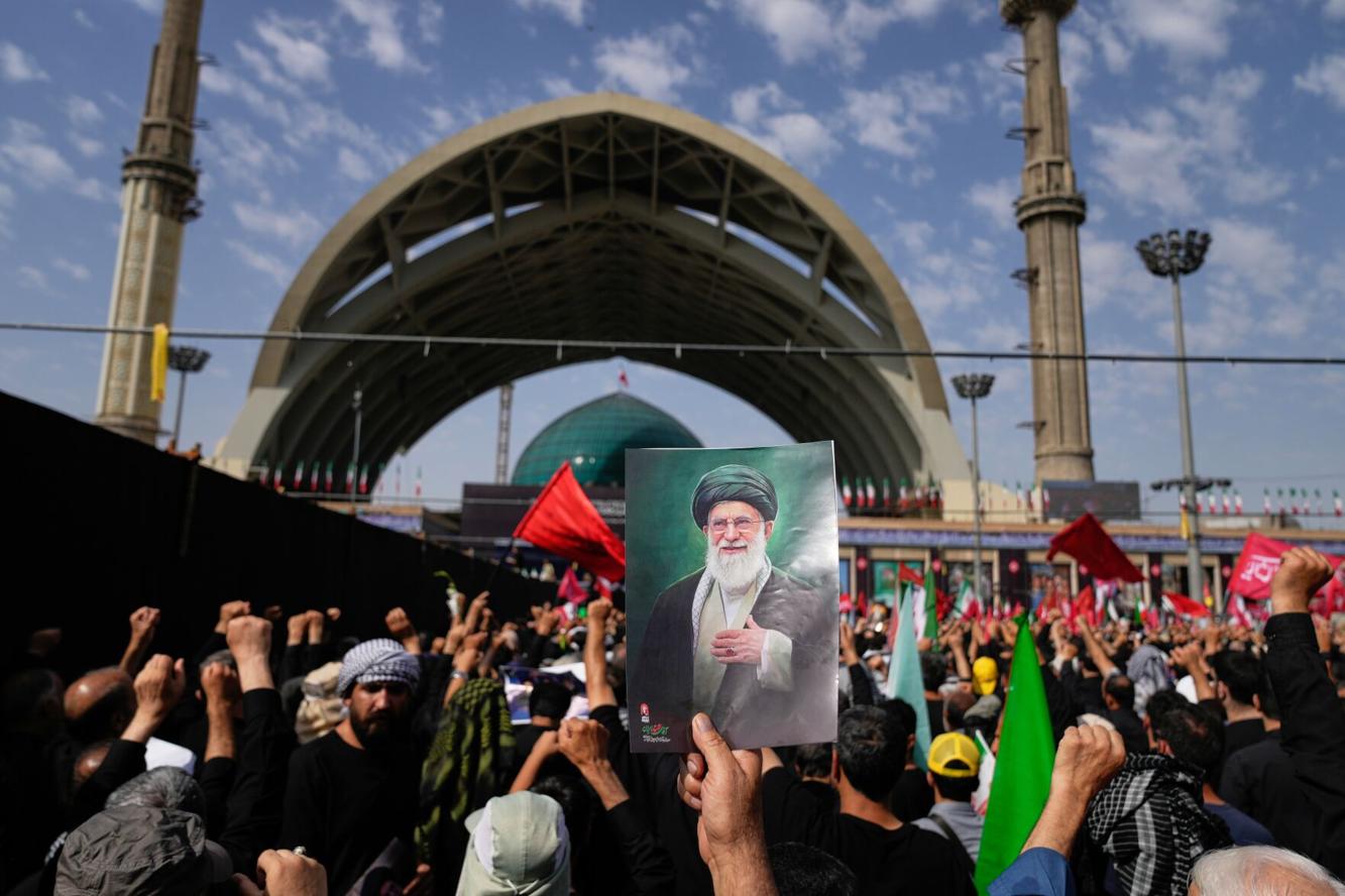 Mourners raise a portrait of Ayatollah Ali Khamenei amidst a large crowd, with fists in the air, during his funeral procession in Tehran.