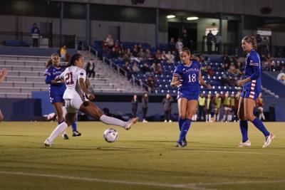 KU women's soccer player shoots the ball between Oklahoma defenders