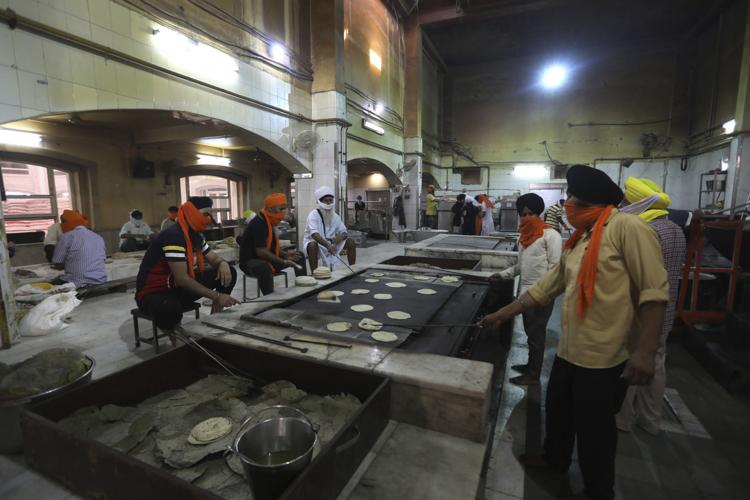 A cook in a Sikh kitchen cooking in an extremely large pot.