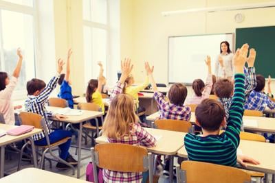group of school kids raising hands in classroom