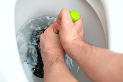 Plumber repairing toilet with hand plunger.