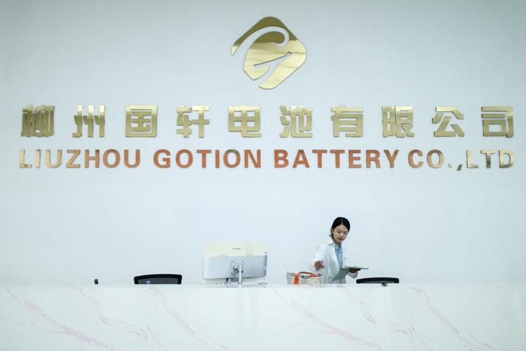 A woman stands next to a logo of Chinese battery maker Gotion, in Liuzhou