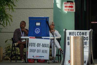 Vote-by-mail attendants sit with a dropbox at the early voting polling site at the Palm Beach County Public Library System Main