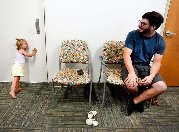 Ty Plumb watches as his daughter Cleo, age 2, tries to listen to her sister’s hearing test through the testing room door Aug. 25 at Children’s Wisconsin Appleton Clinic in Appleton. In July, the Plumb sisters became the first in the nation to receive a