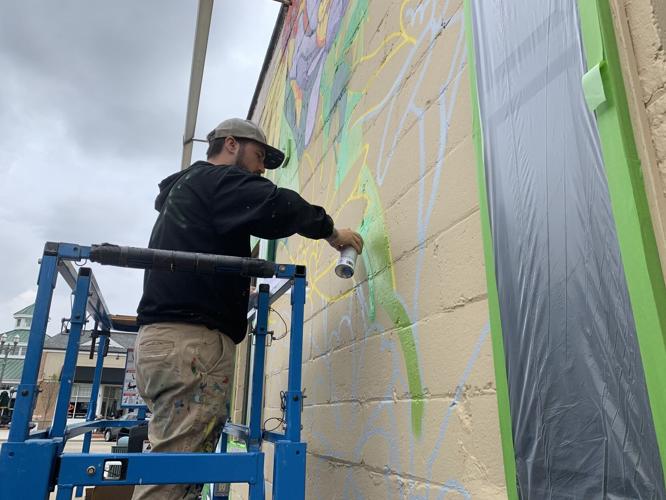 Dustin Eckhardt paints a mural depicting local area flowers on the Christine's Gift building
