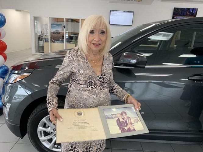 Eileen Fricke stands next to her new Mary Kay car while holding up a photo of a previous car she won from the company