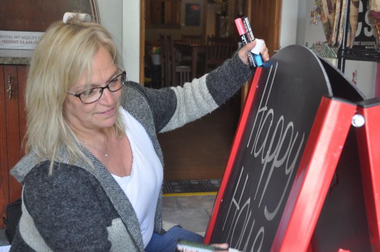 Beth Tumas, owner of the Bottle Shop, writes a sandwich board sign at her business