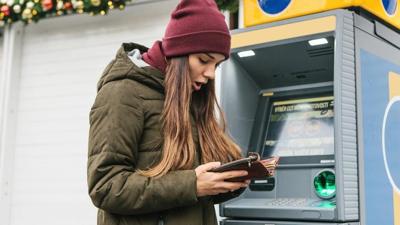 Woman at ATM beneath holiday decorations is shocked at what she sees in her wallet