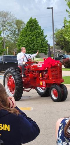 Larry Plapp waves "hi" to his supporters as he rides around on a restored tractor that was presented to him by his students